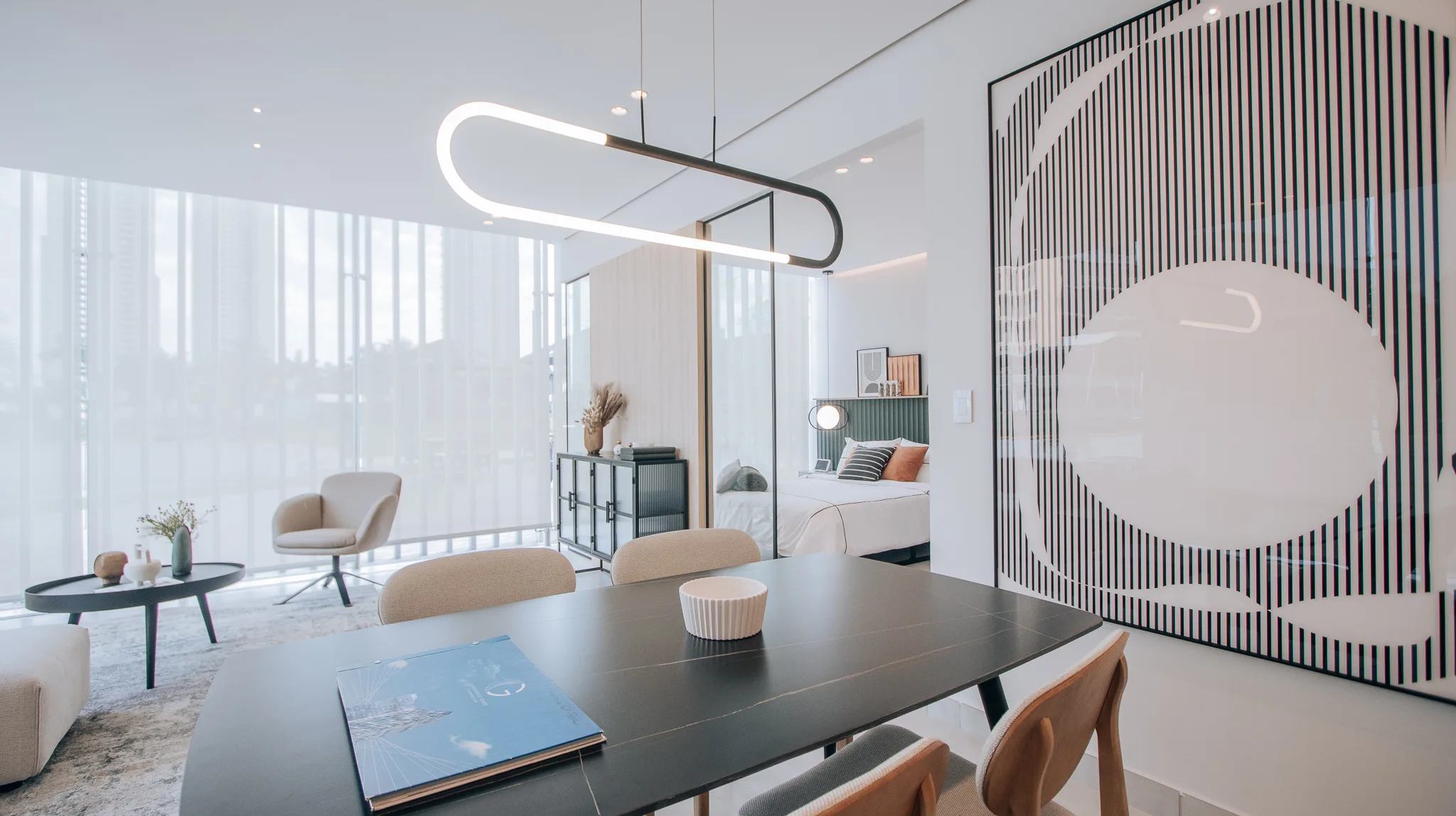 A furnished Generation Tower condo suite, dining table and living area under a looped pendant, the bedroom behind a glass partition and the Costa del Este skyline through full-height windows