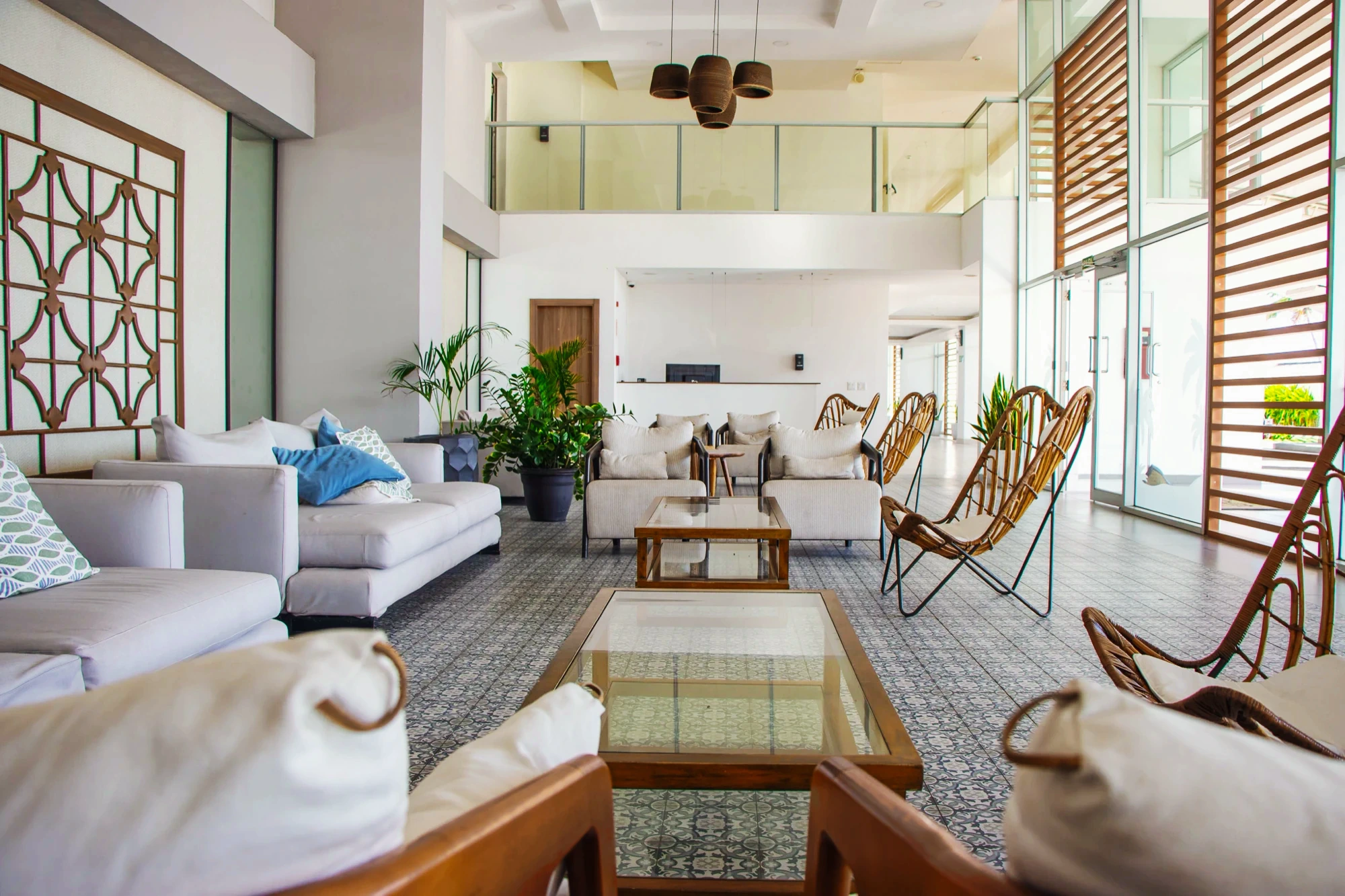 Royal Palm lounge: white sofas, rattan chairs and a glass table on patterned tile under a double-height ceiling