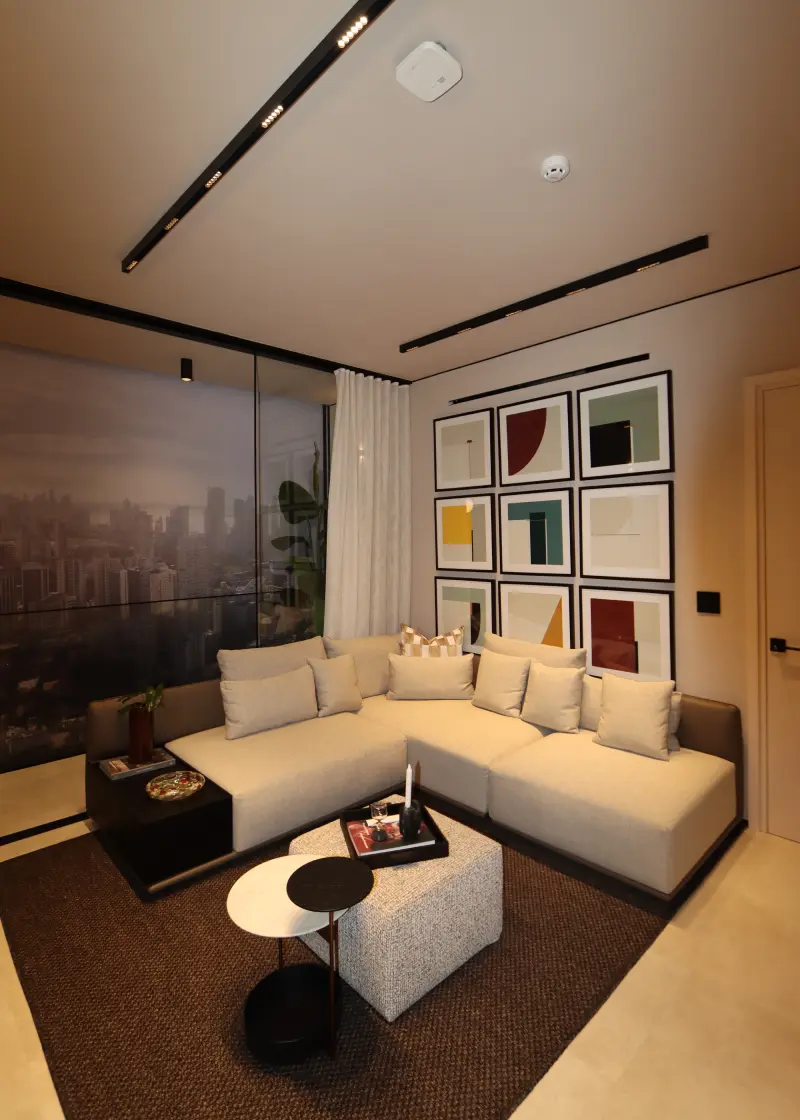 An Uptown living room at dusk, a corner sofa facing a nine-panel art wall, with the Panama City skyline through full-height glass